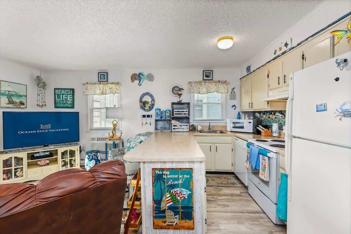 A compact kitchen with a central island, a dining area with a brown leather couch, and a TV on the left.
