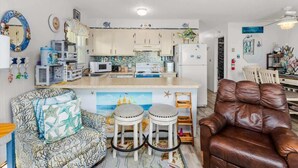 A compact living space with a kitchenette, a sofa, a leather armchair, and a small dining area. - Sunset Shores at Dune Mist (Ocean City)