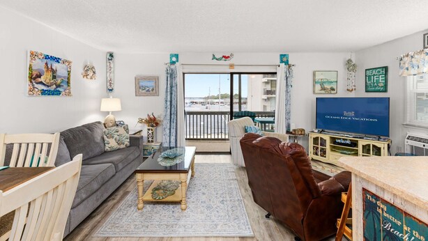 A living room with a sofa, a coffee table, a TV, and a view of the outside. - Sunset Shores at Dune Mist (Ocean City)
