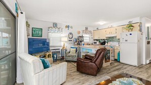 A compact living space with a sofa, a leather chair, a dining table, and a kitchen area. - Sunset Shores at Dune Mist (Ocean City)