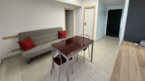 A modern living room with a sofa, a dining table, and a chair. There is a door leading to another room. - Foyer in Bibione With 1 Bedrooms and 1 Bathrooms (San Michele al Tagliamento)