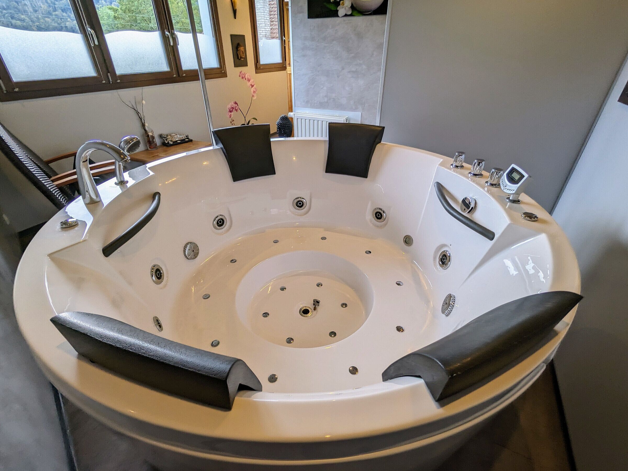 Une salle de bain moderne avec une grande baignoire ronde, un lavabo et une fenêtre laissant entrer la lumière naturelle.