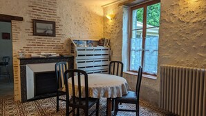 Zona de menjador acollidora amb una taula i cadires, una paret de maó, una finestra amb cortines de galeria i un radiador.