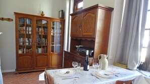 Un comedor con una mesa dispuesta para cuatro, un mueble de madera con puertas de cristal y una zona de cocina con estufa.