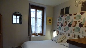 Un dormitorio con cama, una ventana con cortinas, un radiador, una pared con arte abstracto y un aparador.