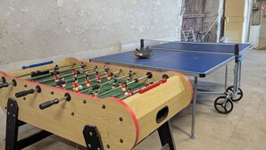 Une table de baby-foot et une table de ping-pong se trouvent dans une pièce aux murs en béton et à la porte en bois.