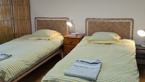 Deux lits simples avec une literie à rayures, une lampe de chevet, une table de chevet en bois et une tête de lit en osier.