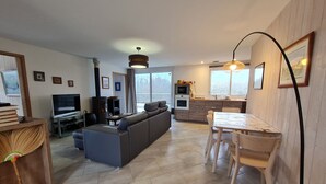 A modern living room with a sofa, TV, and fireplace. There is a dining area with a table and chairs. The kitchen has a microwave and oven. - Cottage in Sologne with leisure and activities nearby (Jouy-le-Potier)
