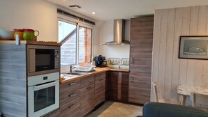 A modern kitchen with a built-in oven, microwave, and a stainless steel range hood. There is a window with a view of the outside, and a dining area with a table and chairs. - Cottage in Sologne with leisure and activities nearby (Jouy-le-Potier)