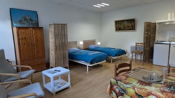 Una habitación con dos camas, un escritorio, una silla, un armario y una mesa de comedor con fruta.