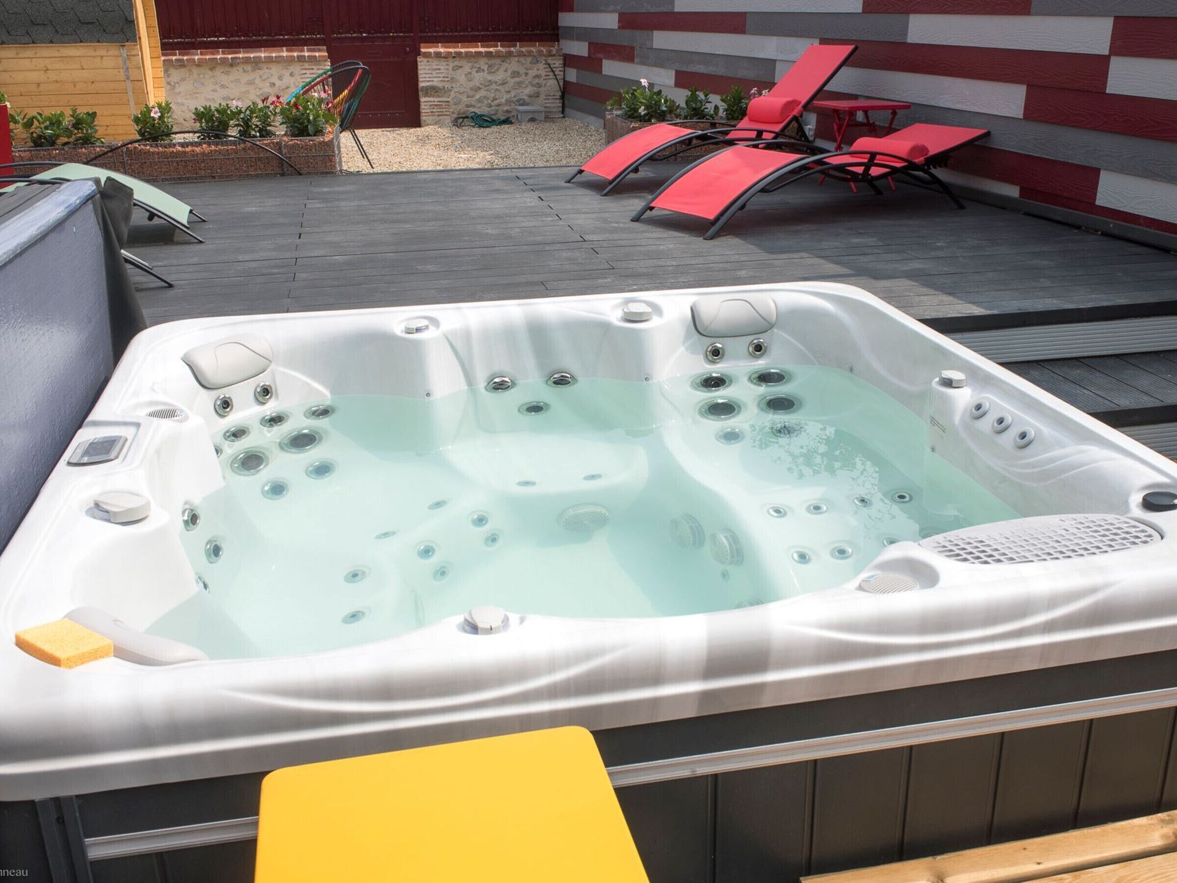 A hot tub with multiple jets, surrounded by outdoor furniture and a stone wall.