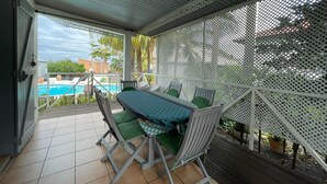 En overdækket terrasse med udsigt til poolen, udendørs møbler og et dekorativt loft.