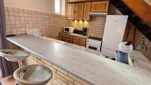 Eine Küche mit einer langen Arbeitsplatte, Holzschränken, einem weißen Kühlschrank und einer Mikrowelle.