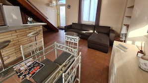 Ein kompakter Wohnbereich mit Küchenzeile, einer Couch, einem Esstisch und einer Treppe zu einer erhöhten Ebene.