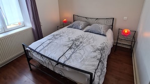 Ein Schlafzimmer mit einem Bett, zwei Nachttischen, einem Fenster mit Vorhängen und einer Heizung.