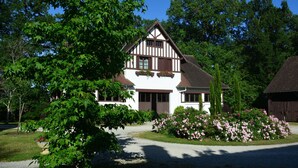 A traditional half-timbered house with a symmetrical facade, a central entrance, and a well-maintained garden with flowering bushes.
