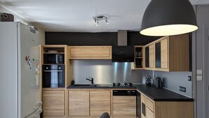 Une cuisine moderne avec des meubles en bois, un four encastré, un lave-vaisselle et une hotte aspirante noire.