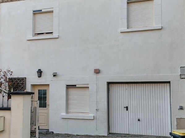 A building with a white facade, a large garage door, and a small window with shutters.