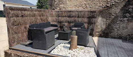 An outdoor seating area with wicker furniture and a decorative tree stump centerpiece, set against a stone wall backdrop.
