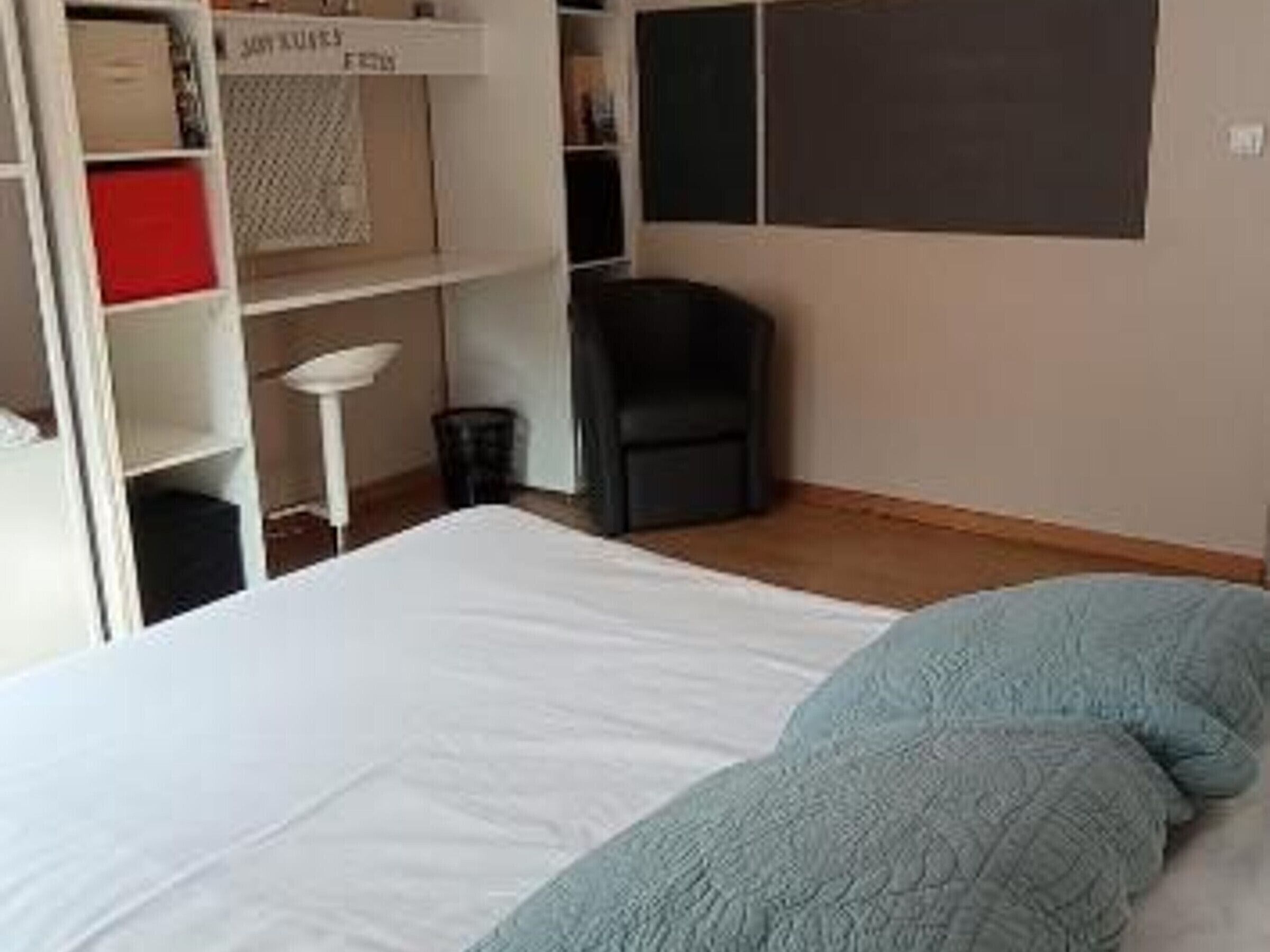 Quarto com cama, poltrona, escrivaninha e estante com caixas organizadoras.