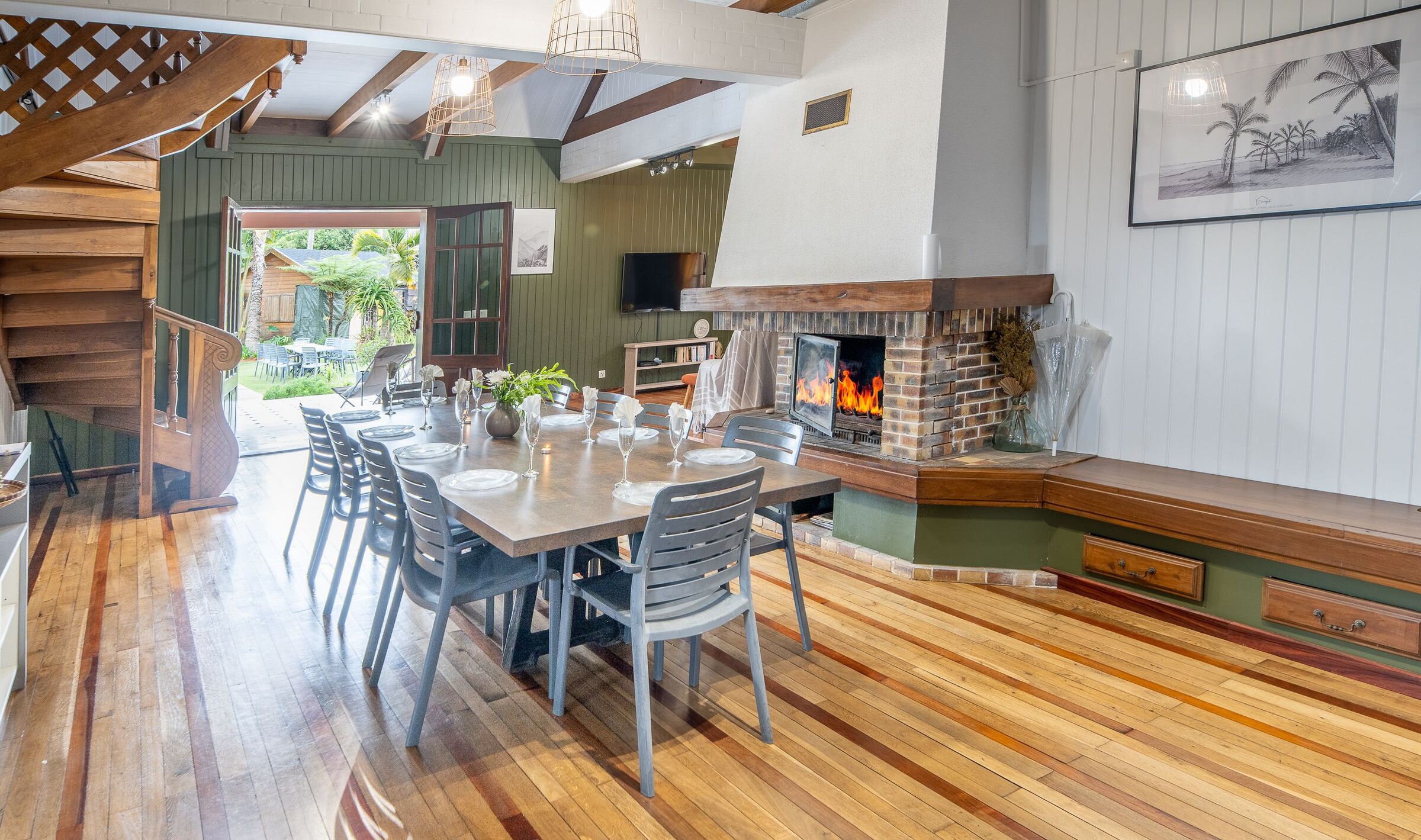A dining area with a brick fireplace, wooden flooring, and a view of the outdoors.