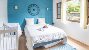 Una camera da letto con una parete blu, un letto con biancheria bianca, una culla, una sveglia e una finestra con tende.