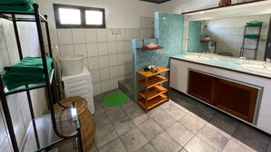 Une petite salle de bain comprenant un lavabo, un miroir et une petite étagère avec des articles de toilette. Un tapis vert est posé sur le sol, et un porte-serviettes contient des serviettes pliées.