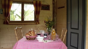 A dining area with a checkered tablecloth, wooden chairs, a basket of bread, a vase with flowers, and a door.