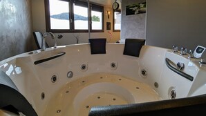 A modern bathroom with a large bathtub, a sink, and a mirror. There are two chairs and a clock on the wall.
