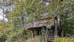 A wooden treehouse with a wooden staircase and a platform, surrounded by dense foliage.