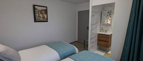 Un dormitorio con dos camas, un baño con pared de mármol y un cuadro en la pared.
