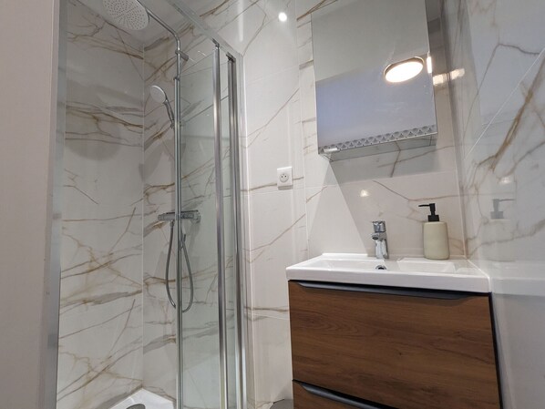 Een moderne badkamer met een douchecabine van glas, een houten wastafelmeubel en een wand betegeld met marmer.