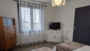 Ein Schlafzimmer mit zwei Betten, einem Fernseher auf einer weißen Kommode, einem Holzschrank und einer Tür.