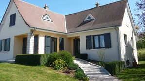 Ein zweistöckiges Haus mit geneigtem Dach, einem Hauseingang mit Stufen und einem kleinen Garten mit gelben Blumen.