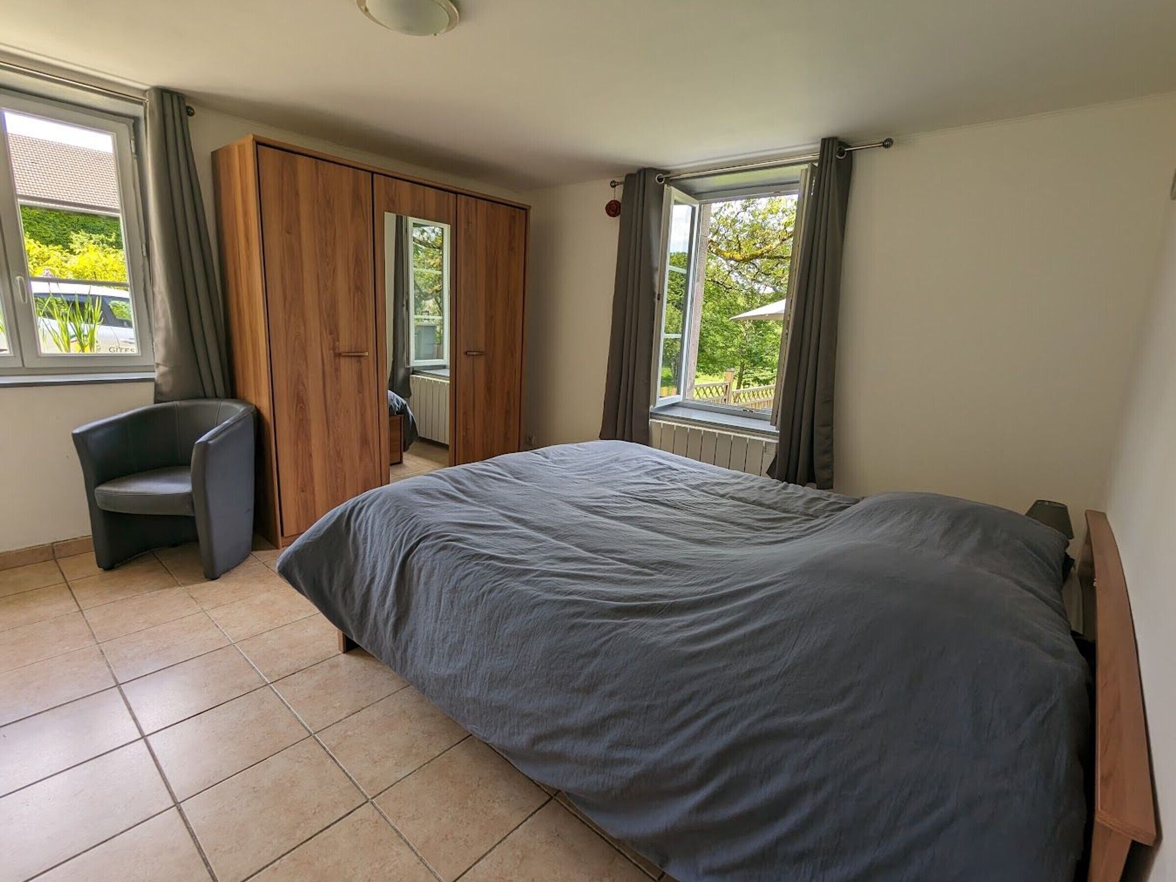 A bedroom with a bed, a chair, a wardrobe, and a window with curtains.