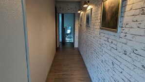 A narrow hallway with white brick walls, wooden flooring, and framed pictures.