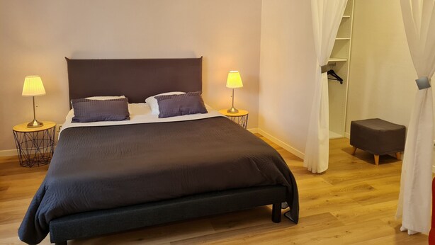 Ein Schlafzimmer mit einem großen Bett, zwei Nachttischlampen, einer Pendelleuchte, einem Kleiderschrank und einem kleinen Hocker.
