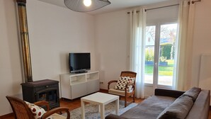 Ein Wohnzimmer mit einer Couch, zwei Sesseln, einem Fernseher auf einem Schrank, einem Kamin und einem großen Fenster.