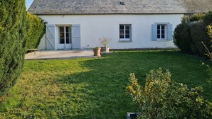 Ein weißes Haus mit einem geneigten Dach, einem Schornstein und einem kleinen Garten mit Rasen und einigen Blumentöpfen.