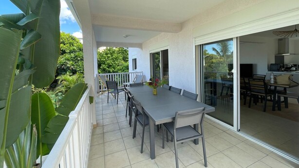 A balcony with a dining table and chairs, a sliding glass door leading to a kitchen, and a view of lush greenery. - Spacious stay in Saint-Louis, perfect for hiking and beach (Saint-Louis)