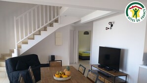 A modern living room with a wooden dining table, a black sofa, a television, and a staircase leading to another room. - Spacious stay in Saint-Louis, perfect for hiking and beach (Saint-Louis)