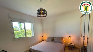 A bedroom with a bed, two bedside lamps, a window, a chair, and a wardrobe. - Spacious stay in Saint-Louis, perfect for hiking and beach (Saint-Louis)