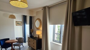 A hotel room with a bed, a desk, a chair, a dresser, a lamp, a mirror, a TV, and a window with curtains. - Large Cottage in Briare - Pets and Private Parking (Briare)