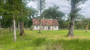 Una casa amb teulada d'argila, envoltada d'un camp verd i arbres.