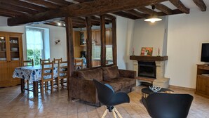 A rustic living room with exposed wooden beams, a fireplace, a dining area with a table and chairs, and a television on a wooden cabinet.
