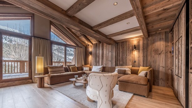 Een ruime woonkamer met een houten plafond en grote ramen, ingericht met banken en een salontafel.
