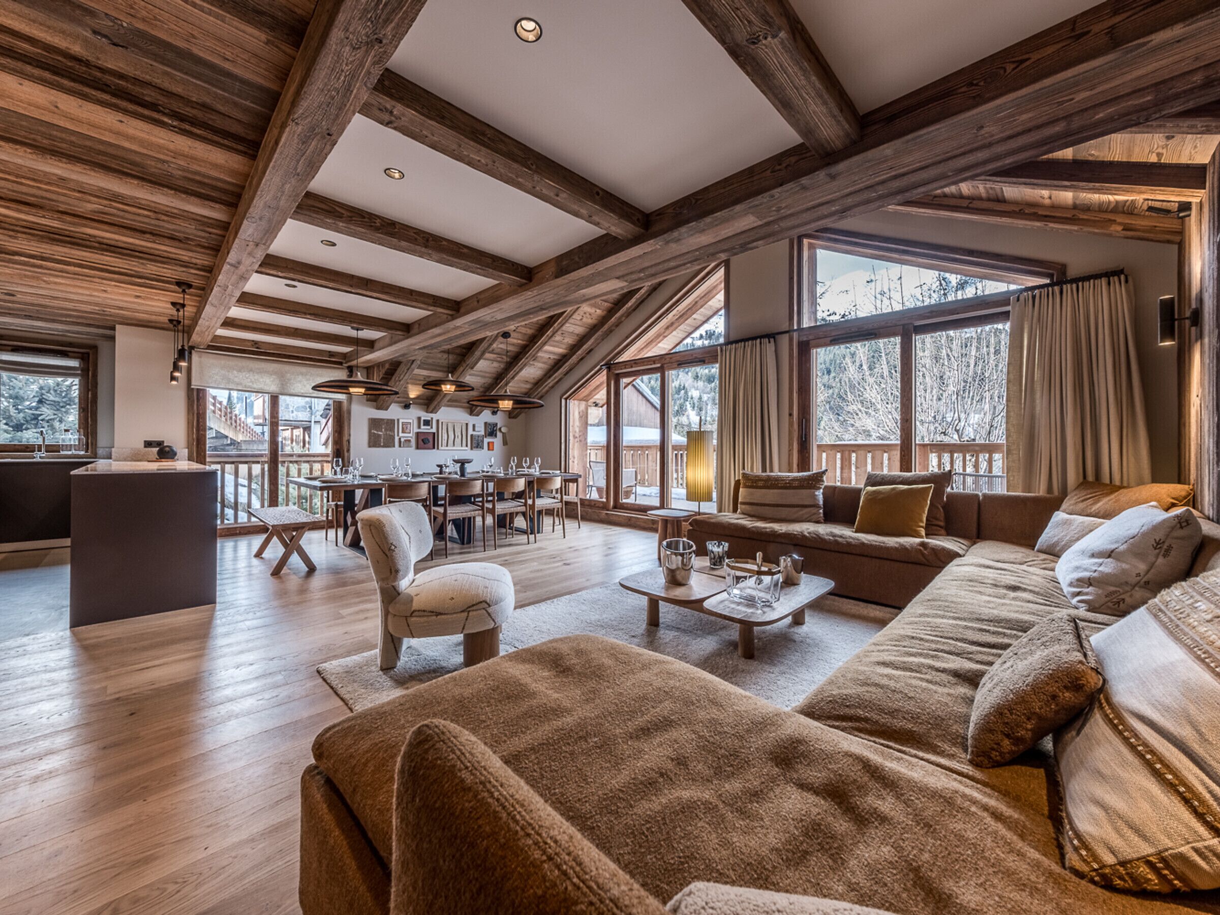 A spacious living area with a wooden ceiling, large windows, a sofa, and a dining area.
