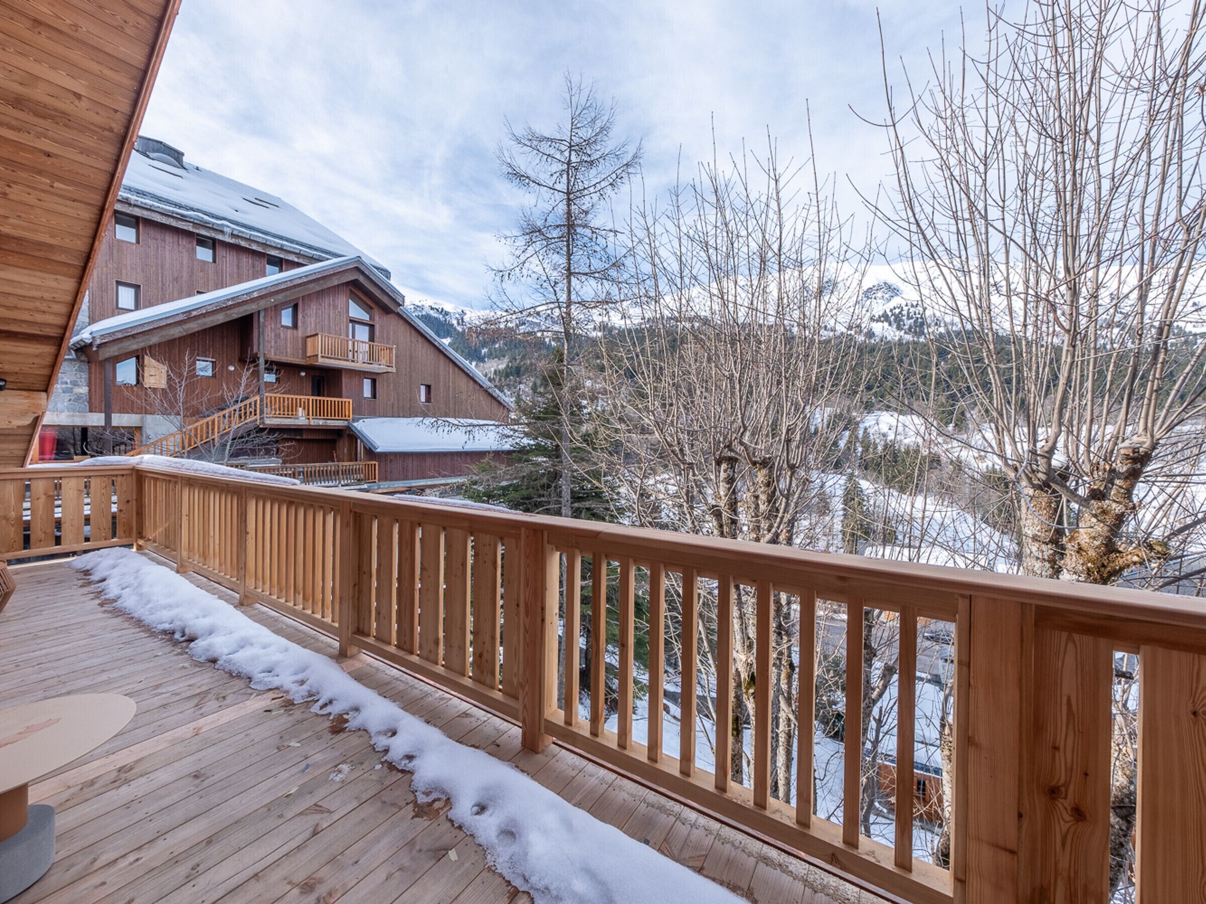 A wooden deck with a railing overlooking a snowy landscape and a building with multiple windows and balconies.