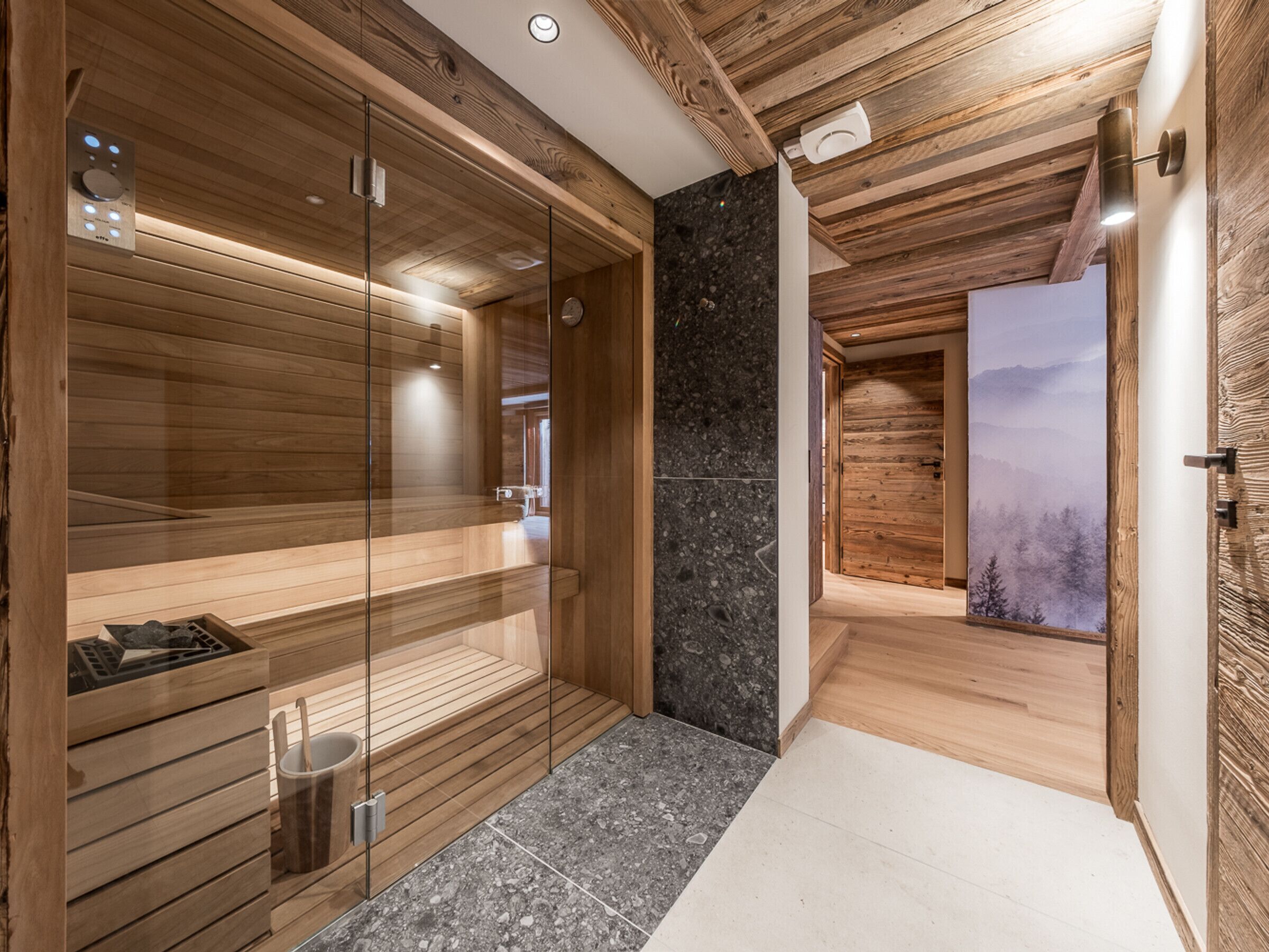 Un sauna moderno con paredes de madera, una puerta de vidrio y vistas a un bosque por la ventana.