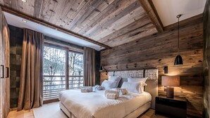 Een moderne slaapkamer met een groot bed, houten plafond en uitzicht op bomen.